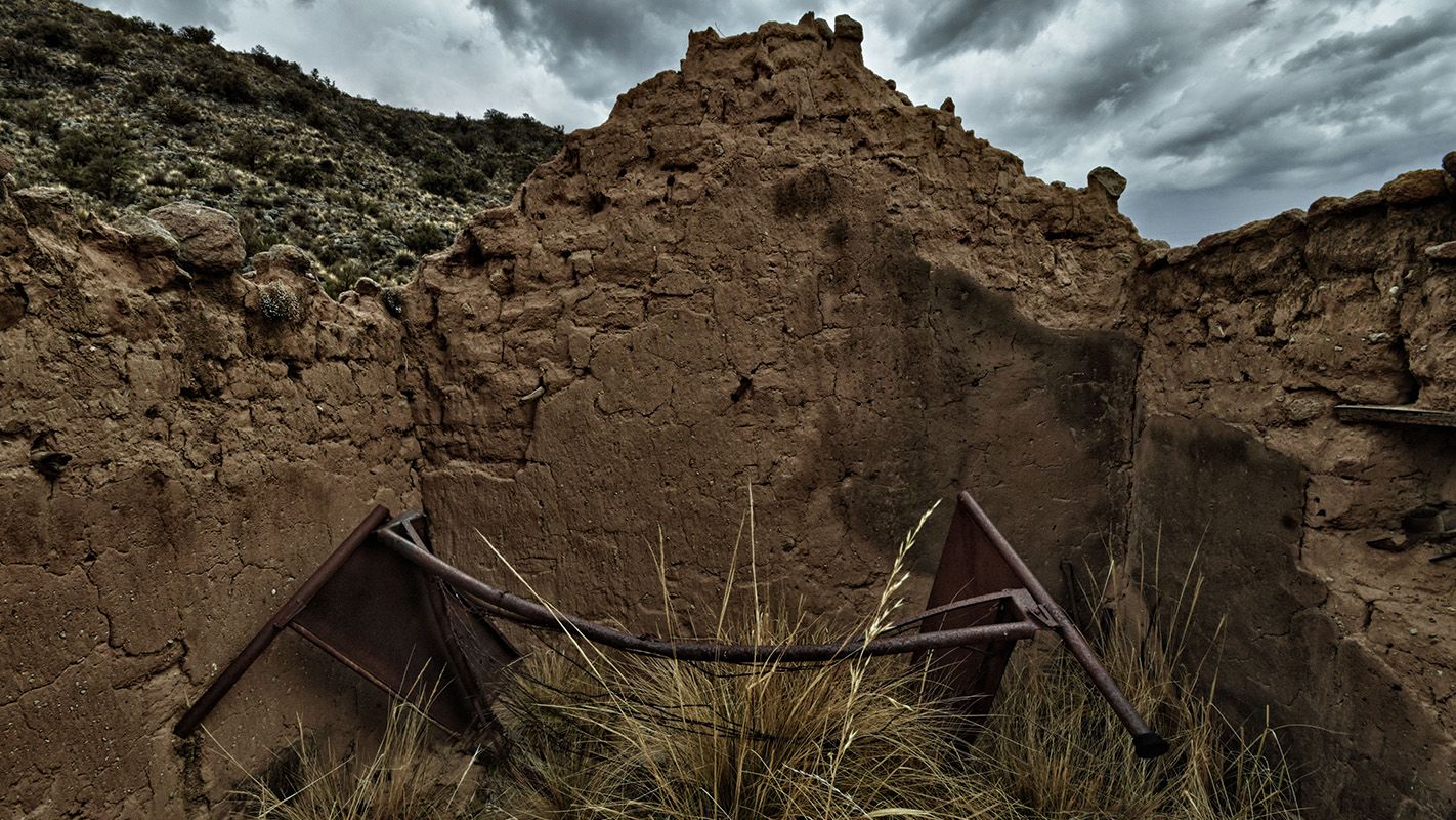 An old, broken bed frame in the middle of the ruins of what used to be a house.