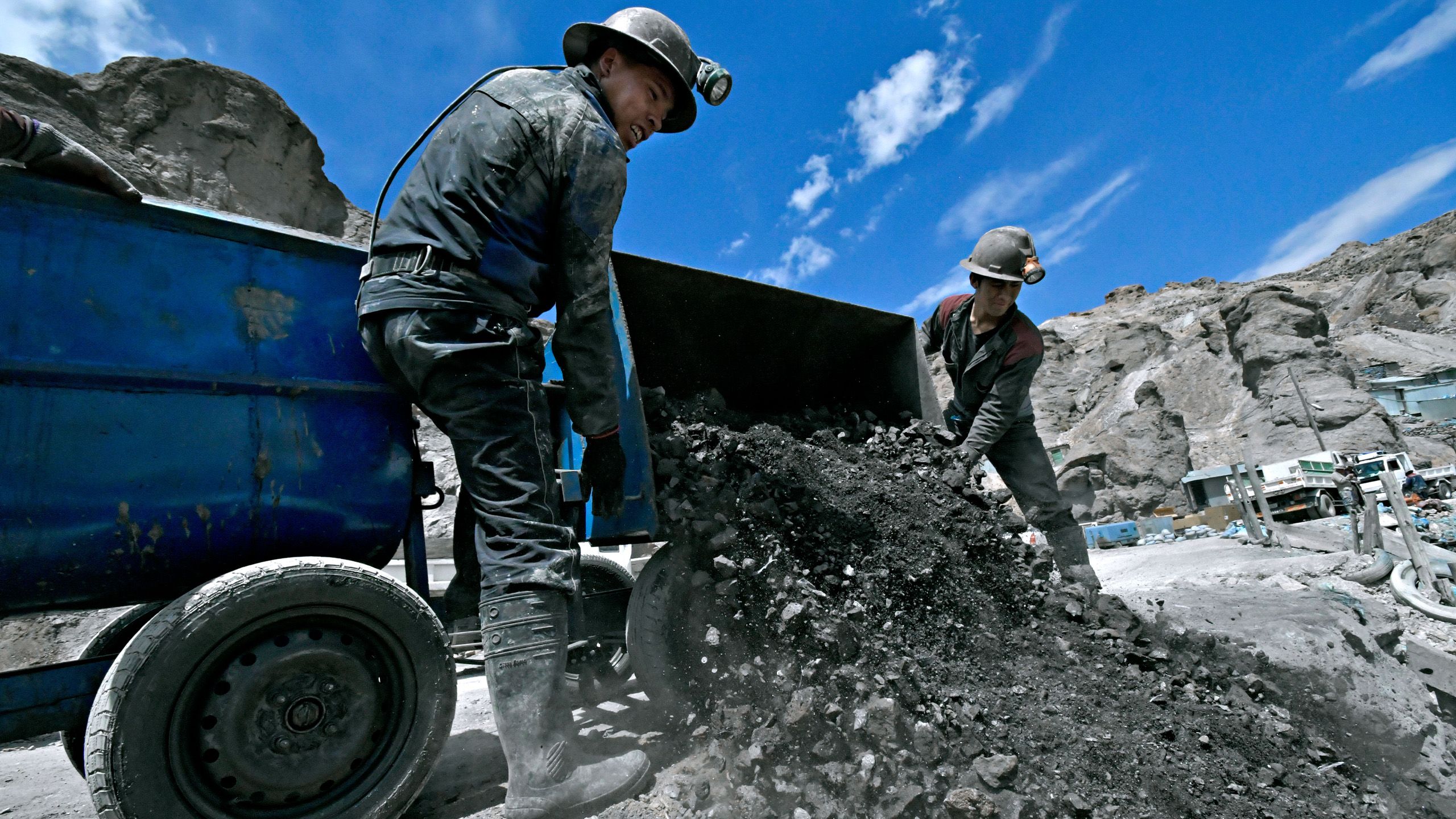Two workers are tilting the trailer and emptying it of boulders and stones.