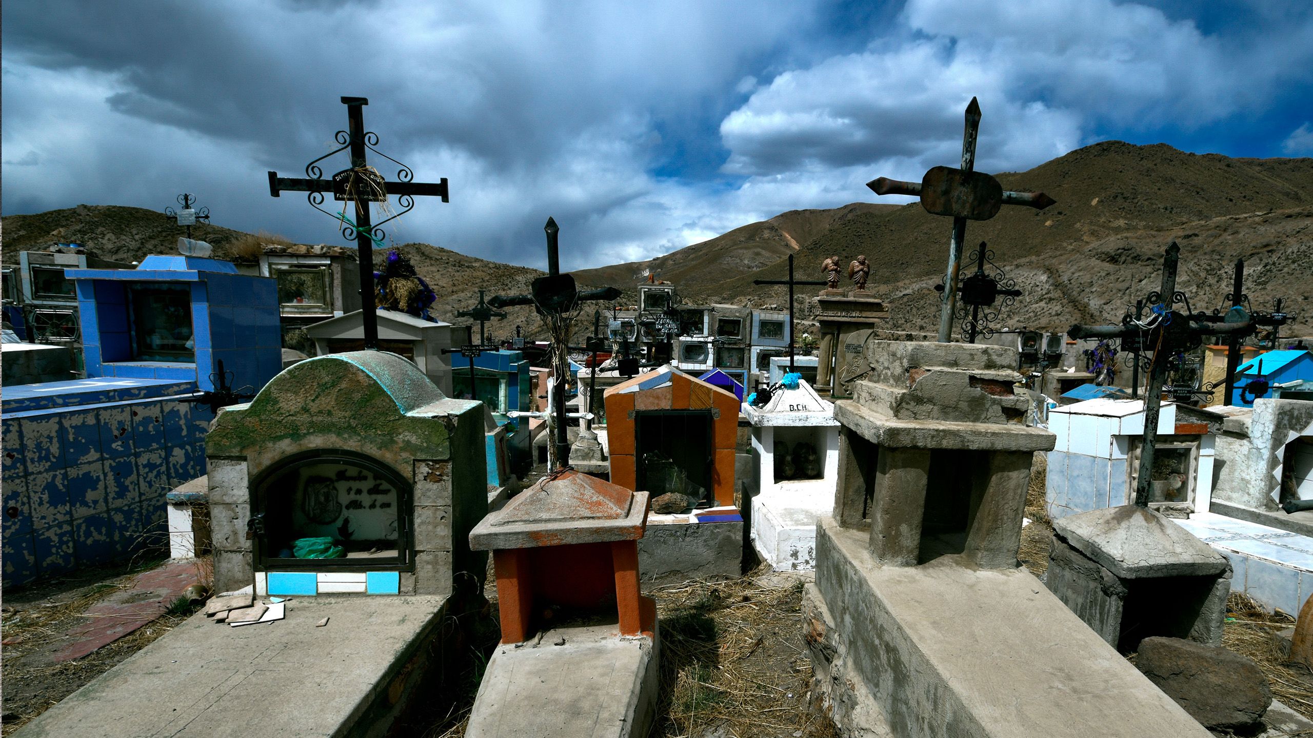 A small cemetery with colorful gravestones in front of barren mountains.