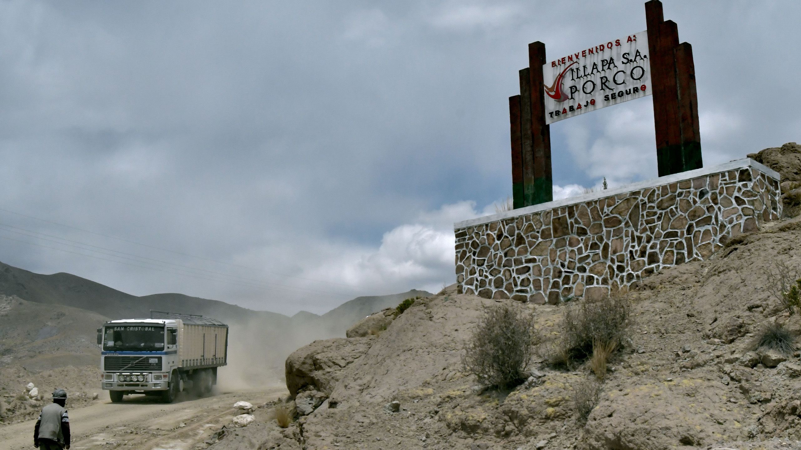 A truck drives on a dusty road under a big sign saying "Illapa S.A. Porco".