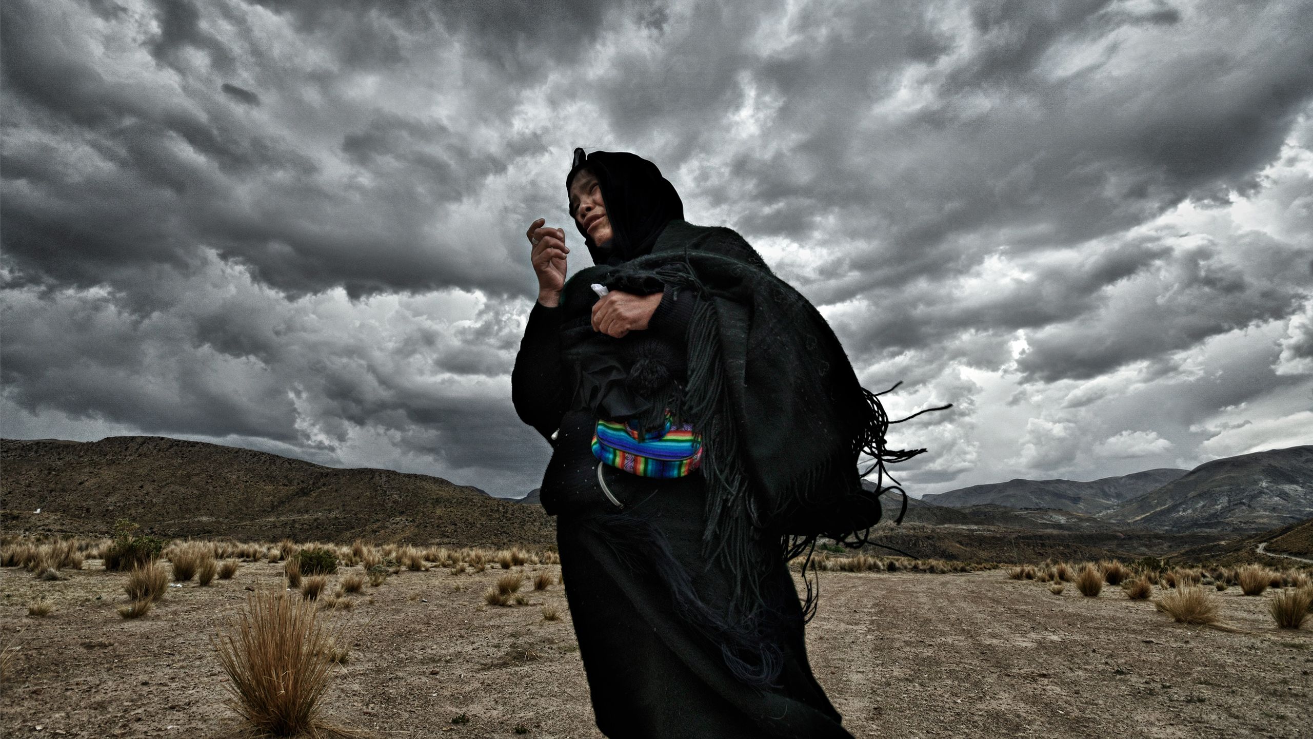 The widow from the first picture in this story stands desperately before dramatic clouds.