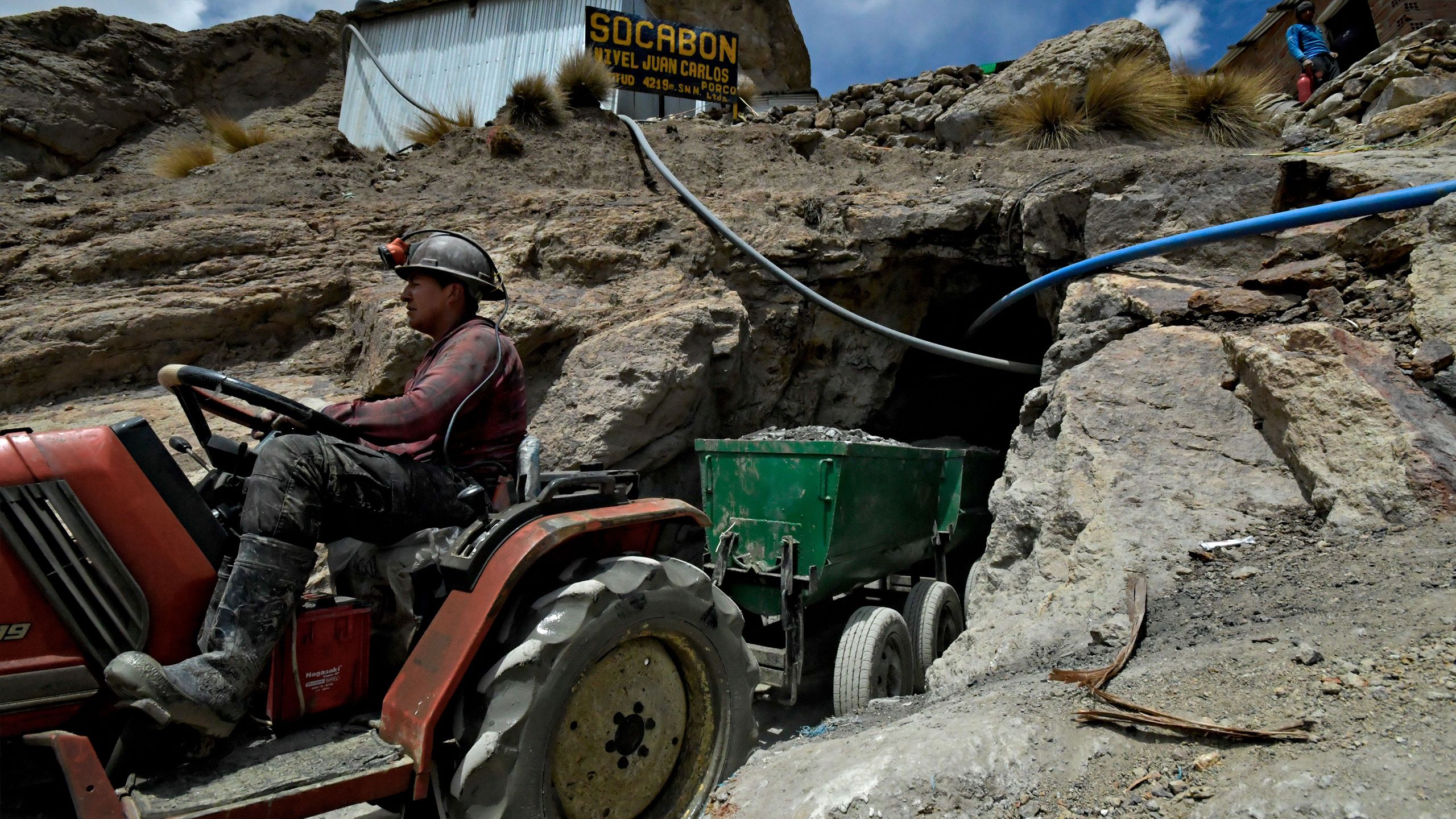 Un ouvrier conduisant un petit tracteur et une remorque pleine de minerais sort du tunnel étroit de la mine.
