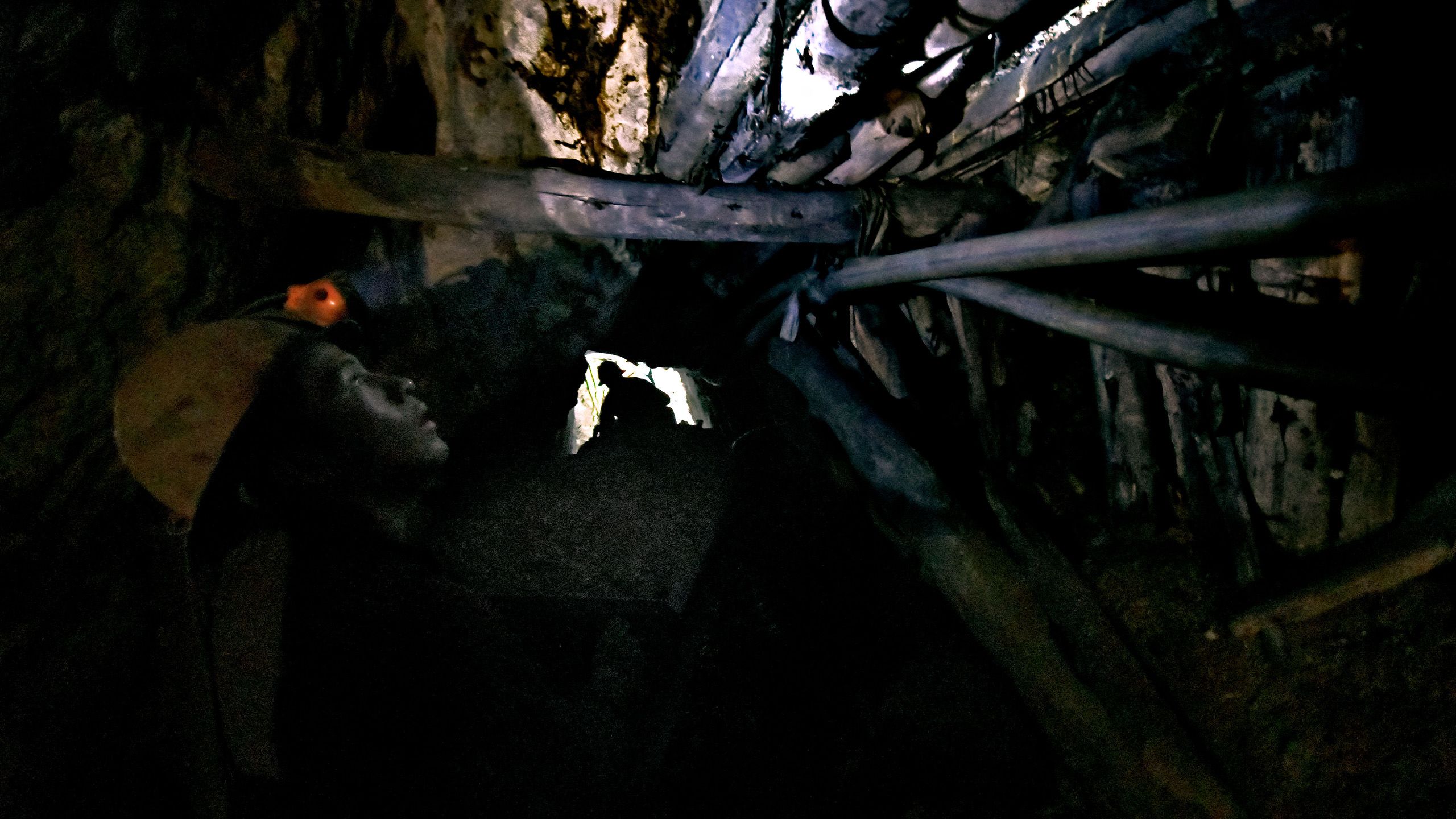 Un travailleur observe le plafond du tunnel et éclaire à la lampe frontale des supports en bois de fortune.